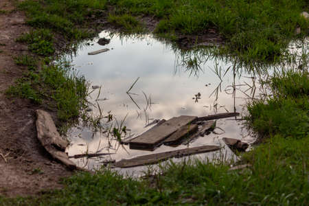A puddle on a muddy road. old boards lie in the waterの写真素材
