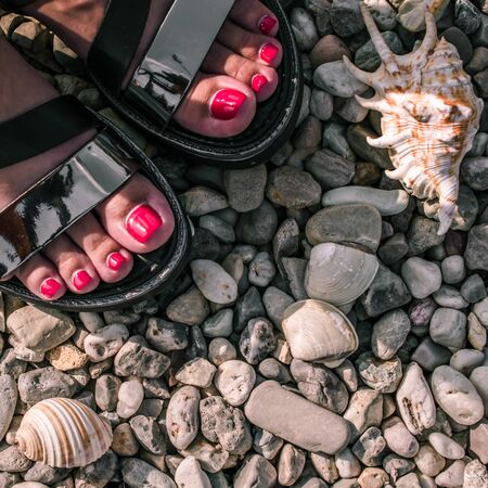 woman with pedicure and sandals on a pebble beachの写真素材