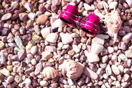 binoculars red or pink on a pebble beach with shellsの写真素材