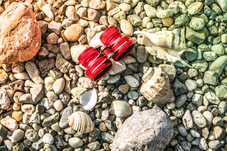 binoculars red or pink on a pebble beach with shellsの写真素材