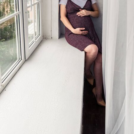 pregnant woman in a dark dress in the interior of a light roomの写真素材