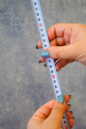 woman holding a measuring tape against a wall backgroundの写真素材