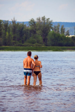 Back view of young couple standing in the water and looking at each otherの写真素材