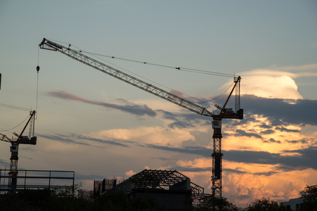 Industrial construction cranes and building silhouettes over sun at sunset.の写真素材