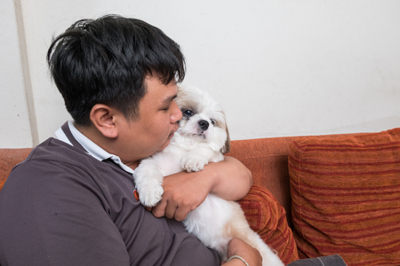 man beautiful young happy with long dark hair in white sweater holding small dog.の写真素材