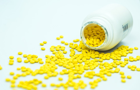 yellow pills spilling out of  medicine bottle isolated on white background.の写真素材