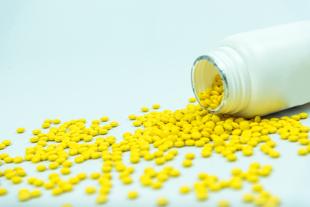yellow pills spilling out of  medicine bottle isolated on white background.の写真素材