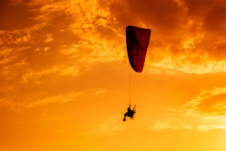Paramotor flying on the sky at sunset.Paramotor silhouette on the orange skyの写真素材