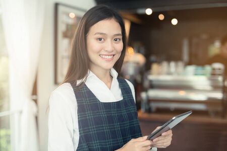 Asian woman barista smiling with tablet in her hand,Female employees are taking orders from online customers.,Warm photos at the coffee shopの写真素材