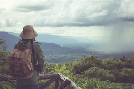 Hipster young woman with backpack enjoying. Tourist traveler on mountain background,Photographers carrying a camera stand looking at the rain on the mountain.の写真素材