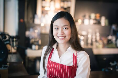 Asian female barista wears red apron standing in a cafeの写真素材
