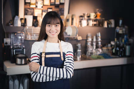 Asian female barista wears blue apron standing in a cafeの写真素材