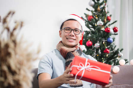 Asian man sitting on sofa holding gift box,christmas day conceptの写真素材