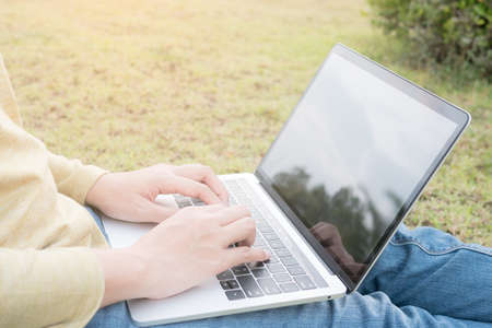 Asian women using laptop on green lawn.