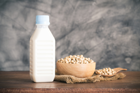 Soy milk in bottle and soybean in wood bowl on wooden tableの写真素材