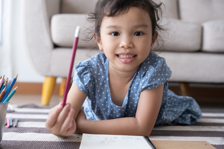 The girl  holding a pencil and smiling, aisan girl are drawing and happily at homeの写真素材