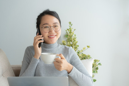 Asian working woman on her face wear glasses , smile , talk on telephone .Young business woman is...