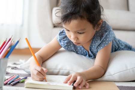 Cute little girl drawing homework and writing with pen on paper in her homeの写真素材