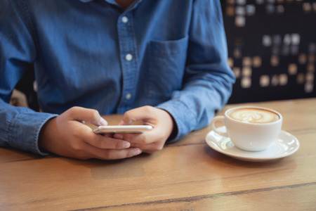 Hand of asian woman using smartphone on wooden table in coffee shopの写真素材