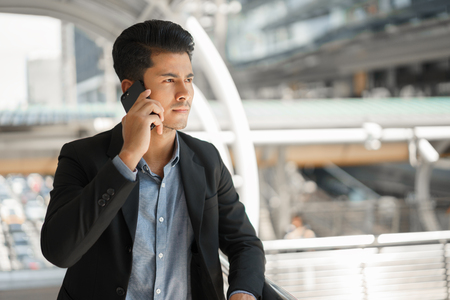 Portrait of asian young businessman standing at Outside Office. A man wear suit so smart and talking on  smartphone to business conversation.の写真素材