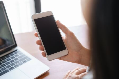 Close up hand using smartphone on desk background in office.  On hand holding smartphone blank display.の写真素材