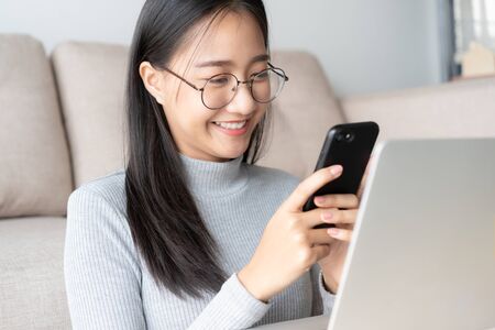 Beautiful young Asian women are using smartphone to chat with friend. Asian girl using smartphone for video call in the living room at home.の写真素材