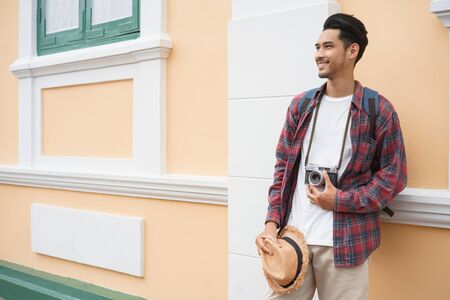Handsome Asian man tourist Standing at wall While holding a straw hat at Attractions in Bangkok,...