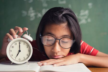 Asian girl is sleeping at the desk in the classroom, The little girl wearing glasses clutches after falling asleep in class.の写真素材
