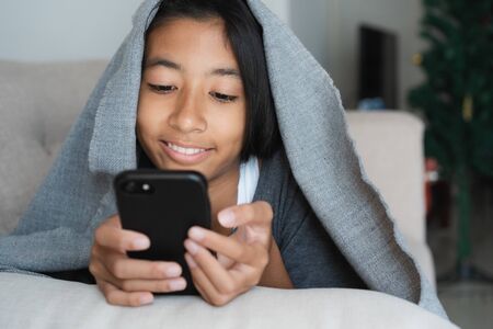 Asian kid girl are watching video that are joking on online media. The little girl using the smartphone to watch video for entertainment on sofa at homeの写真素材