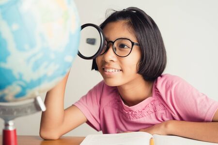 Asian girl wearing glasses is smiling and using a magnifying glass in the classroom, Educational conceptの写真素材