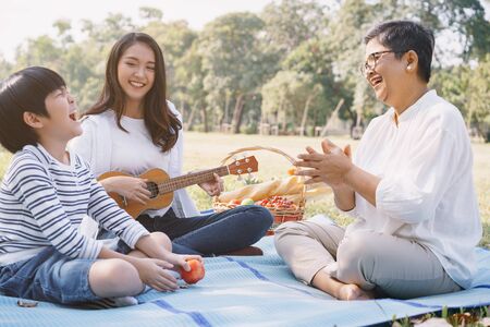 Happy Asian family having fun and enjoying  while playing ukulele in the park. The concept of lifestyle in family holidayの写真素材