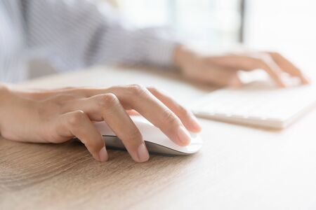 Close up of business woman hand typing on computer keyboard with the mouse while sitting working on the desk in the office or work from homeの写真素材