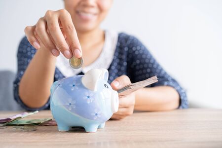 Asian woman hand is putting a coin in a piggy bank and banknote on the table at home, Investment business and retirement.の写真素材
