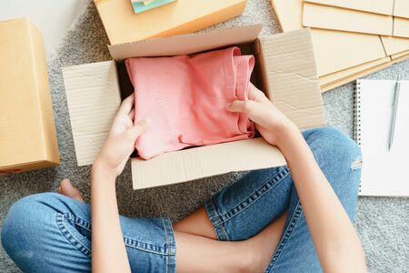 Top view of Asian girl is preparing pink clothes down inside a parcel box according to the customer...