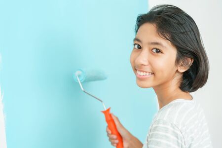 girl Asian painting wall with the paint roller Close-up, Hand of young child renovation or decorating the interior home with the color blue. Close-up child happy smile on the faceの写真素材