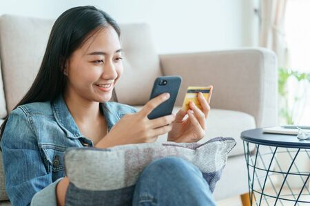 Beautiful young Asian women are buying online with a credit card at home. Women are using a smartphone and doing online transactions. concept of shopping online by technology and lifestyle new normalの写真素材