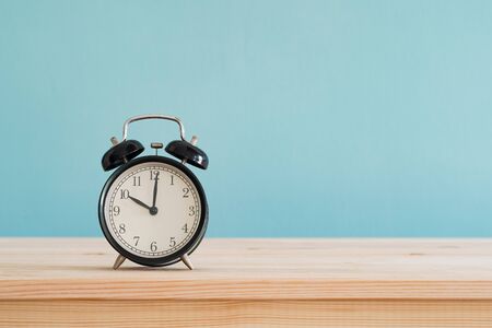 black alarm clock on brown wood desk and blue wallpaper textured background with copy space   の写真素材