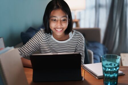 Happy Asian girl is studying online with tablet at desk at night, Asia child smile and expression emotion cheerful on the face her. Concept of online learning at homeの写真素材