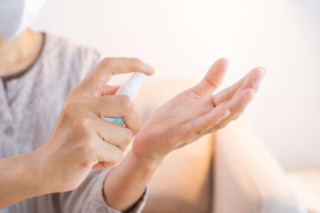Asian women clean hand with alcohol  sanitizer spray prevent the spread of germs and bacteria and avoid virus covid-19 at homeの写真素材