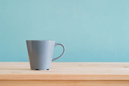 Coffee mugs place on brown wood desk and blue wallpaper textured background with copy space