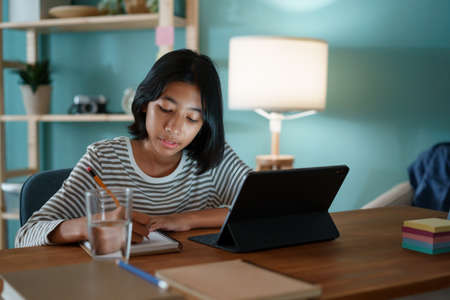 Homeschooling Asian girl doing homework And study online with tablet at a desk at night.