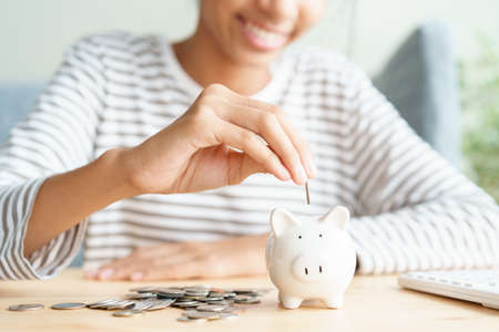 Hand of  Asian young girl are putting coins in a piggy bank at home, Close up of child happy smile, retirement, finance and saving money for future conceptの写真素材