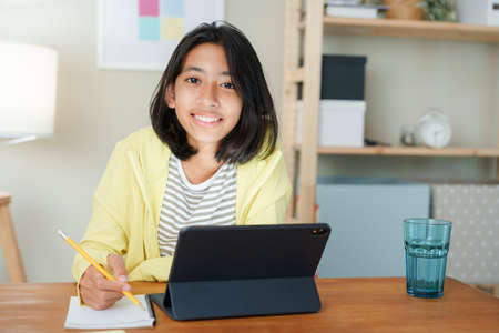 Homeschooling Asian girl doing homework And study online with tablet at the desk night. Portrait of Asia child happiness and smiling confidence looking to cameraの写真素材