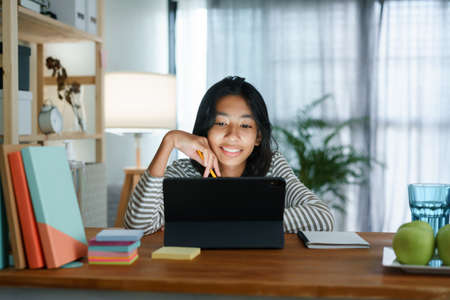 homeschooling. Asian girl learning with the online tutor on the  tablet while sitting on table house nightの写真素材