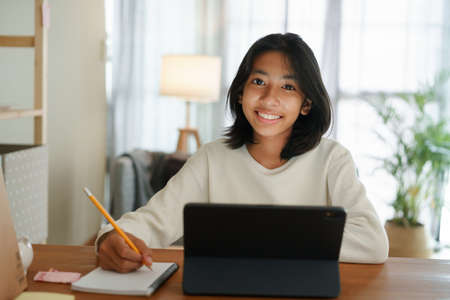 Homeschooling Asian girl doing homework And study online with tablet at the desk night. Portrait of Asia child happiness and smiling confidence looking to cameraの写真素材