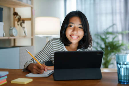 Homeschooling Asian girl doing homework And study online with tablet at the desk night. Portrait of Asia child happiness and smiling confidence looking to cameraの写真素材