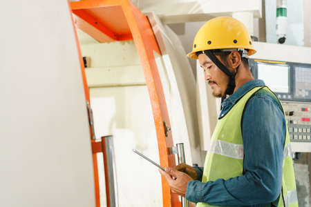 side view of man engineer working on machine and check with tablet digital in the factoryの写真素材