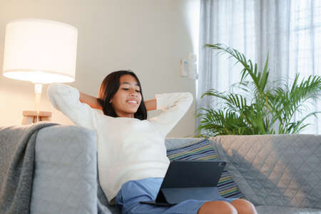 Happy Asian girl using a tablet digital while  sitting on the sofa in the  living room at night