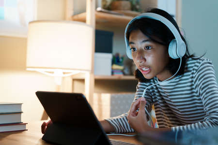 Asian girl study learning online via the internet on tablet with headphones on desk at night home....