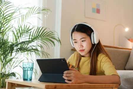 beautiful Asian young woman using a tablet and eat salad for lunch on table work at home. concept working from homeの写真素材